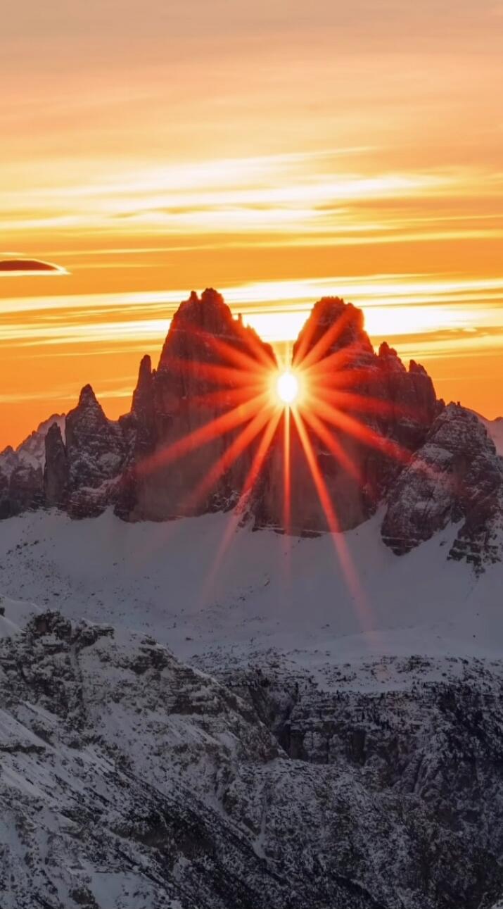 The sun is setting behind the mountains, casting a warm glow over the snowy landscape.