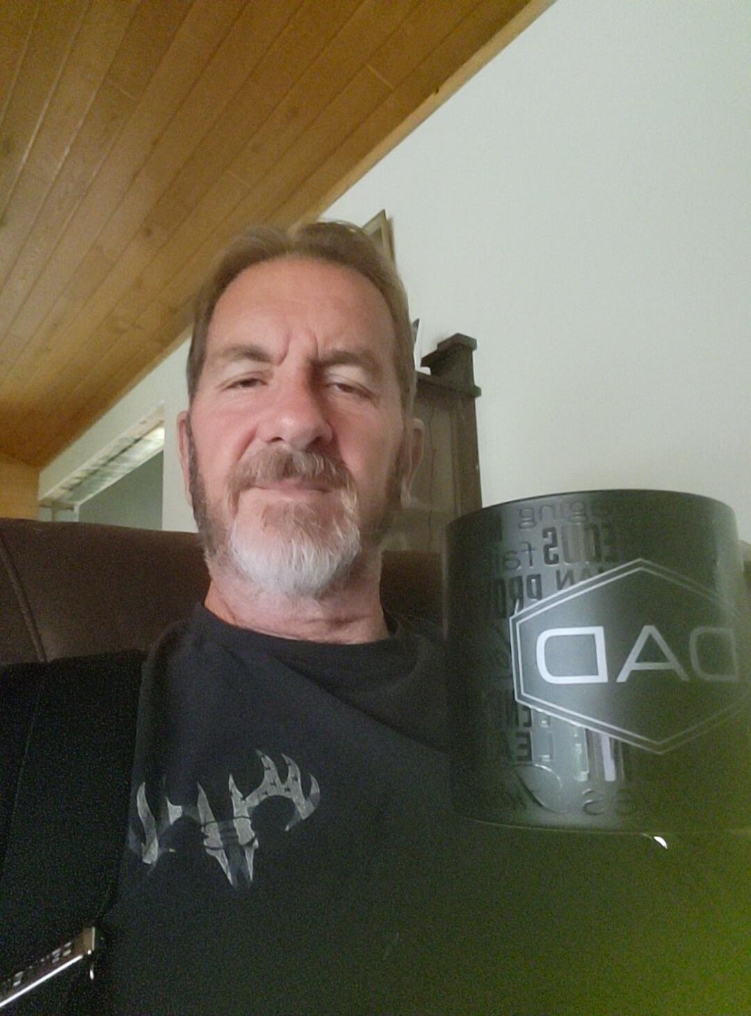 A man holding a black mug with 'DAD' and 'EST. 2003' written on it.