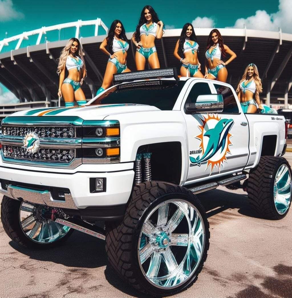 A white lifted pickup truck with teal and orange Miami Marlins-themed graphics, parked at a stadium, surrounded by women in bikinis posing on and beside the vehicle.