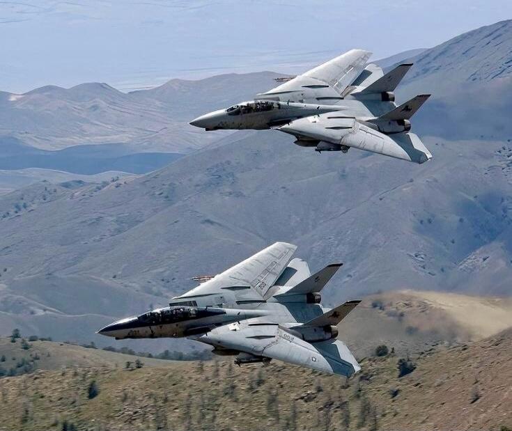 Two fighter jets flying over rugged mountain terrain.