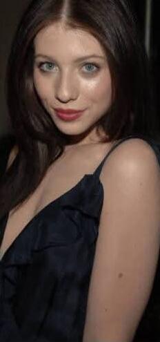 A portrait of a young woman with blue eyes and dark hair, wearing a navy dress with a plunging neckline.