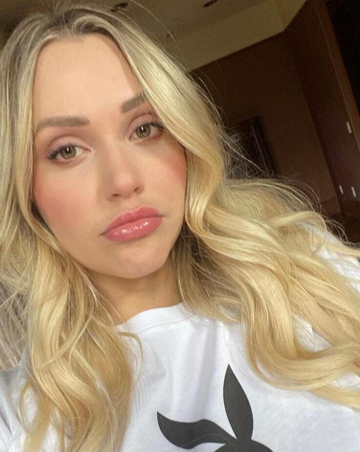 A blonde woman wearing a white t-shirt with a black Playboy bunny logo.