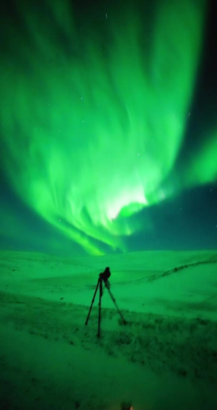 Aurora borealis over snow with a camera on a tripod.