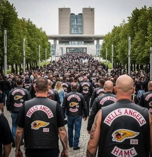 Hells Angels patches on biker jackets read 'HELLS ANGELS' and 'HAMC'. A large crowd of motorcyclists walks down a wide path toward a building.