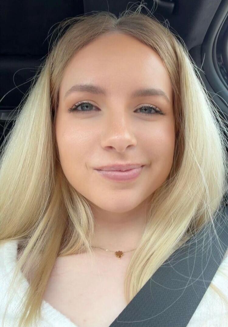 A young woman smiling in a car taking a selfie.