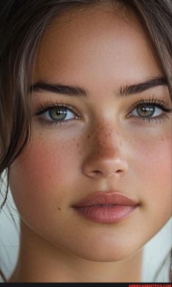 Close-up portrait of a person with green eyes, freckles, and soft pink lips.
