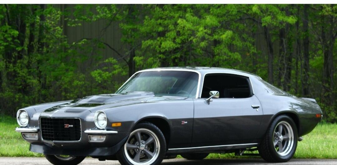 A classic grey Chevrolet Camaro Z28 parked outdoors with green trees in the background.