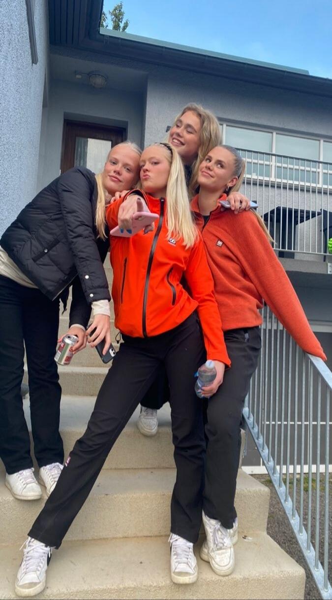 Four young women posing together on outdoor stairs, smiling and making a playful pose.