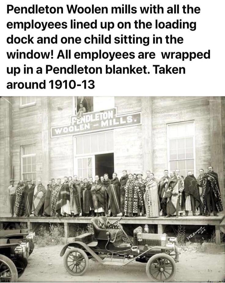 Pendleton Woolen mills with all the employees lined up on the loading dock and one child sitting in the window All employees are wrapped up in a Pendleton blanket Taken around 1910 13 1