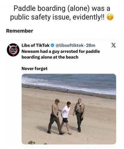 Paddle boarding (alone) was a public safety issue, evidently!! Remember Libs of TikTok Newsom had a guy arrested for paddle boarding alone at the beach Never forget. The image shows two officers escorting a man in handcuffs on a sandy beach near the ocean.