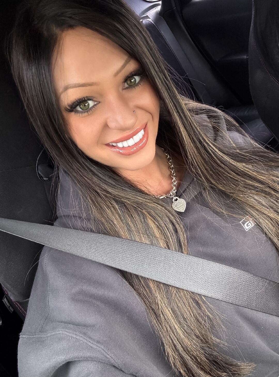Smiling woman in a car, wearing a seatbelt.