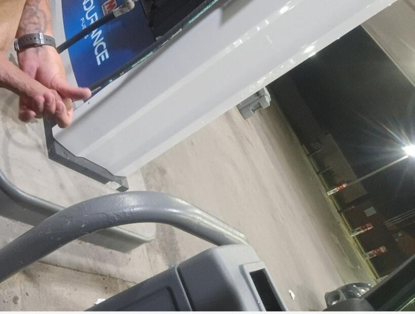 A person's hand is seen holding a part of a fuel pump at a gas station. The text 'DURANCE FUE' is visible on the pump's blue panel.