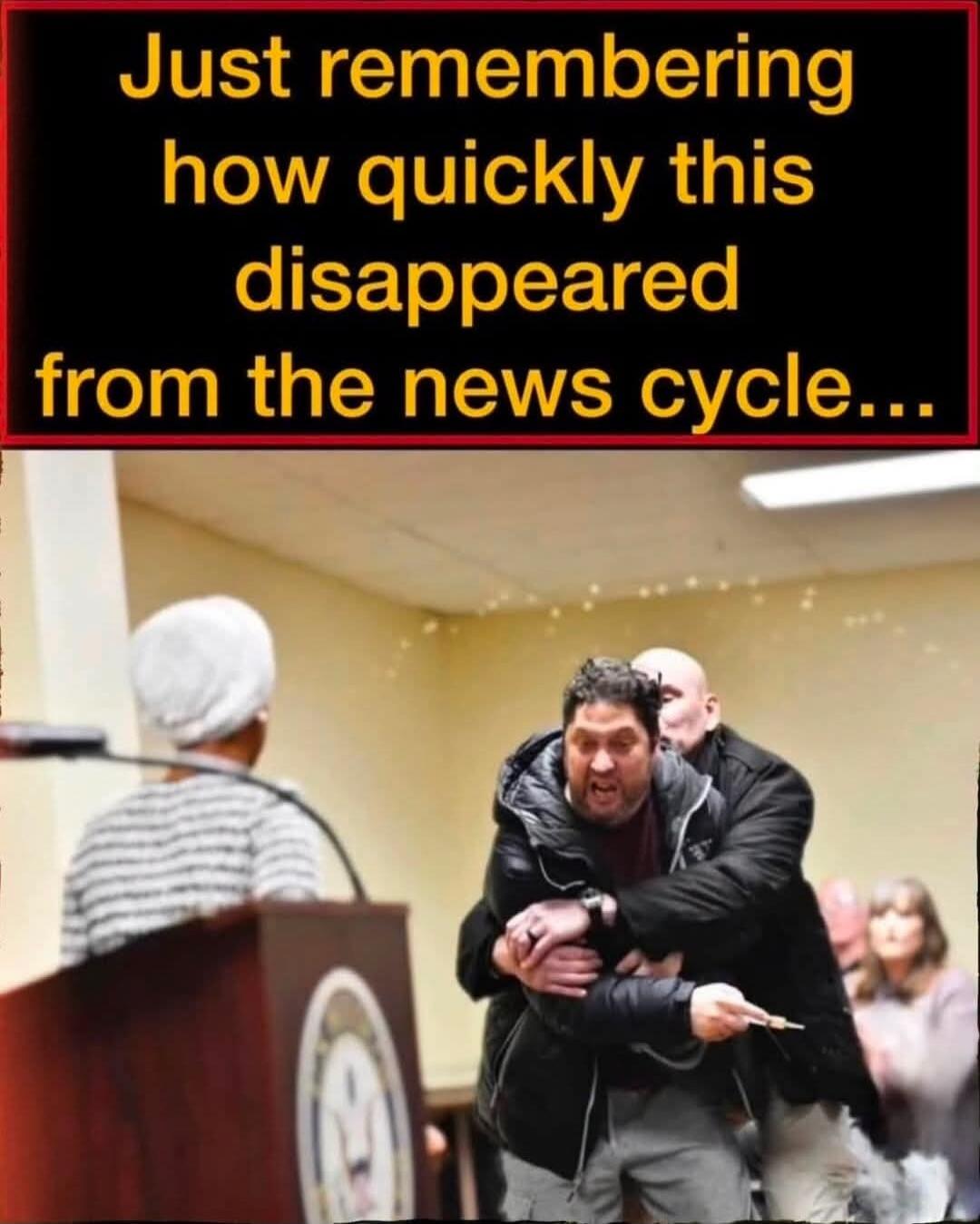 Just remembering how quickly this disappeared from the news cycle... A man is being restrained by another man during what appears to be a public meeting. The restrained man looks distressed and is holding a small, sharp object.