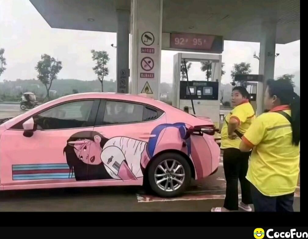 Pink cartoon-decorated car at gas station with damaged rear wheel; two people in yellow shirts observing.