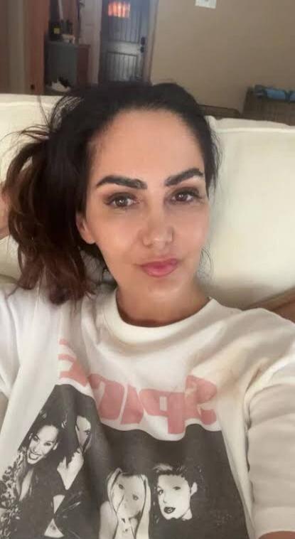 A woman is taking a selfie. She is wearing a white t-shirt with a graphic print that includes the word 'SPICE'.
