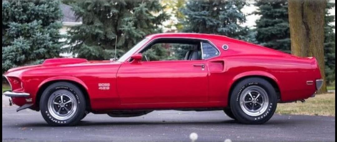 A red classic Ford Mustang Boss 429 car is parked outdoors. The text 'BOSS 429' is visible on the side, and 'GOODYEAR' is on the tires.