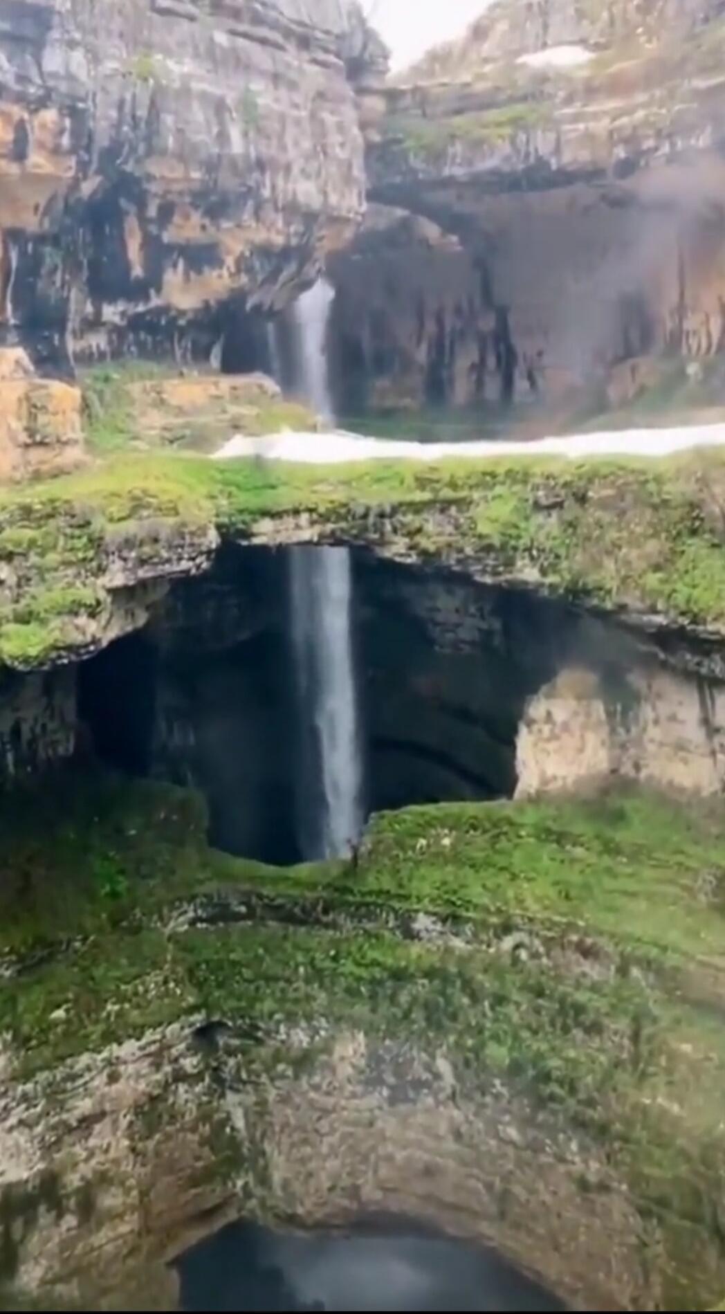 A tall waterfall in a rocky canyon with mossy green cliffs and layered rock formations.