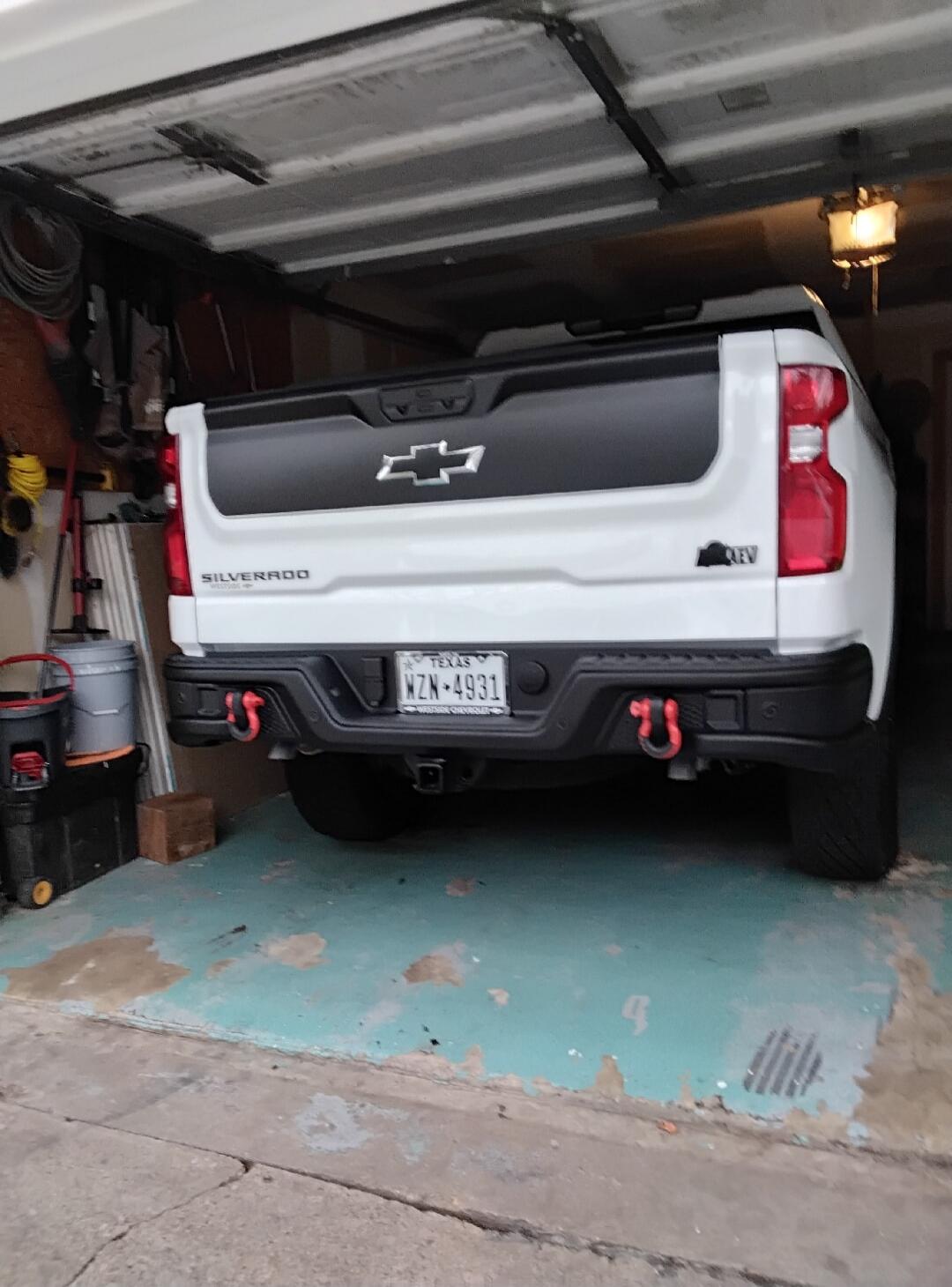 Chevrolet Silverado pickup truck parked in a garage. License plate: TEXAS WZN-4931. Red tow hooks are visible on the bumper.