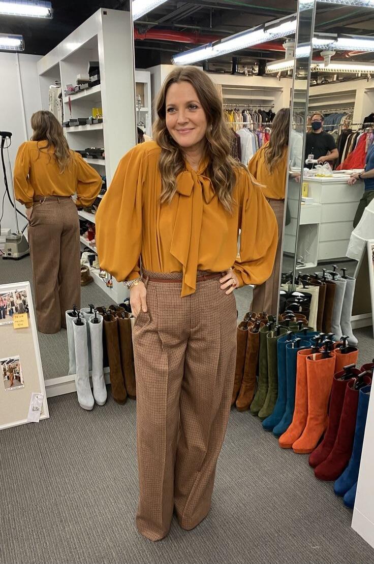 Drew Barrymore posing in a clothing store with many boots.