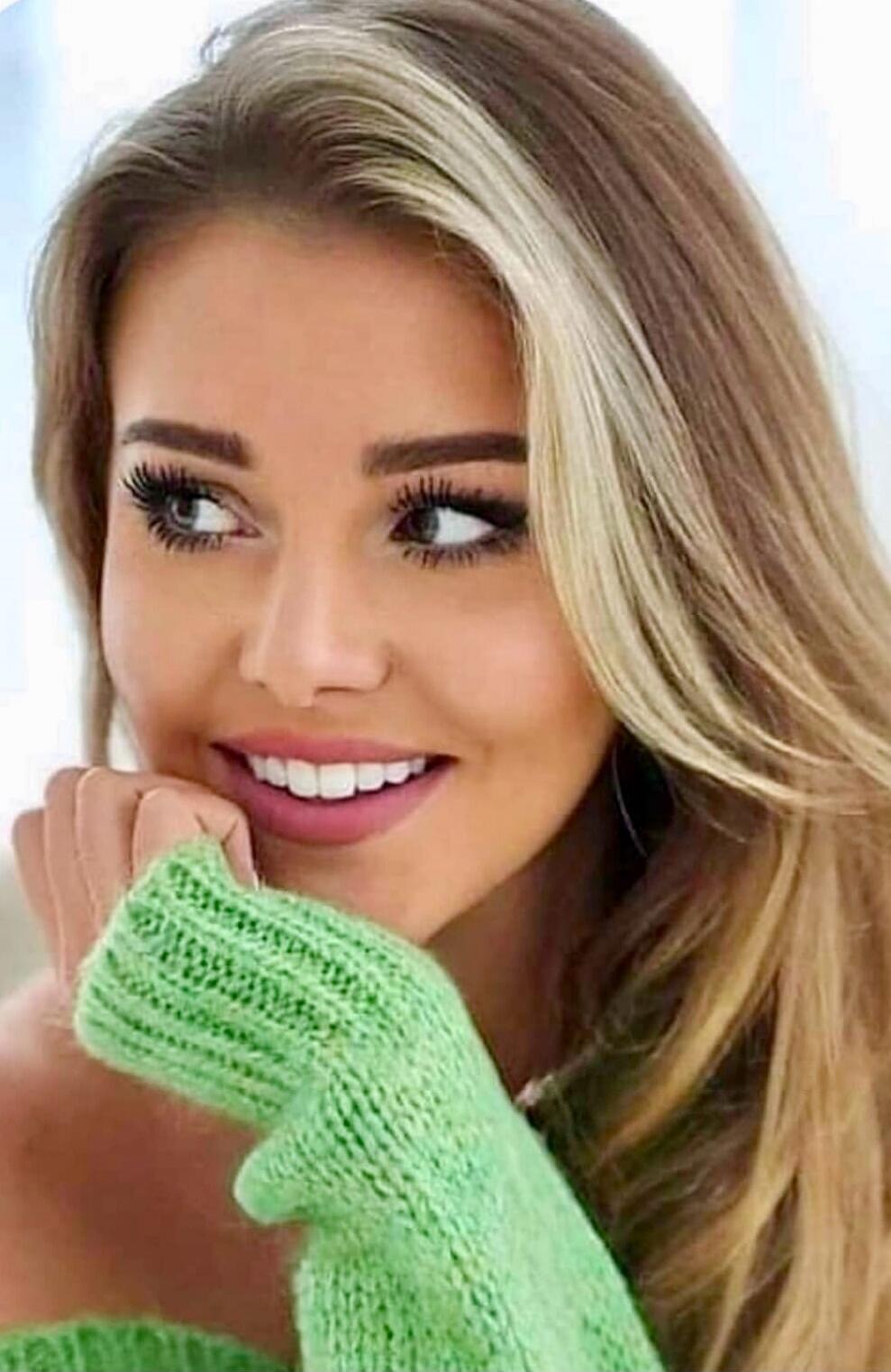 A close-up portrait of a smiling woman wearing a green knit sweater.