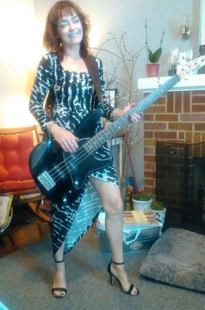 A woman posing with a black bass guitar indoors.