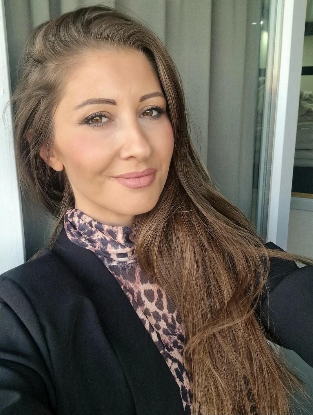 Portrait of a woman taking a selfie, wearing a leopard print top and a black blazer.