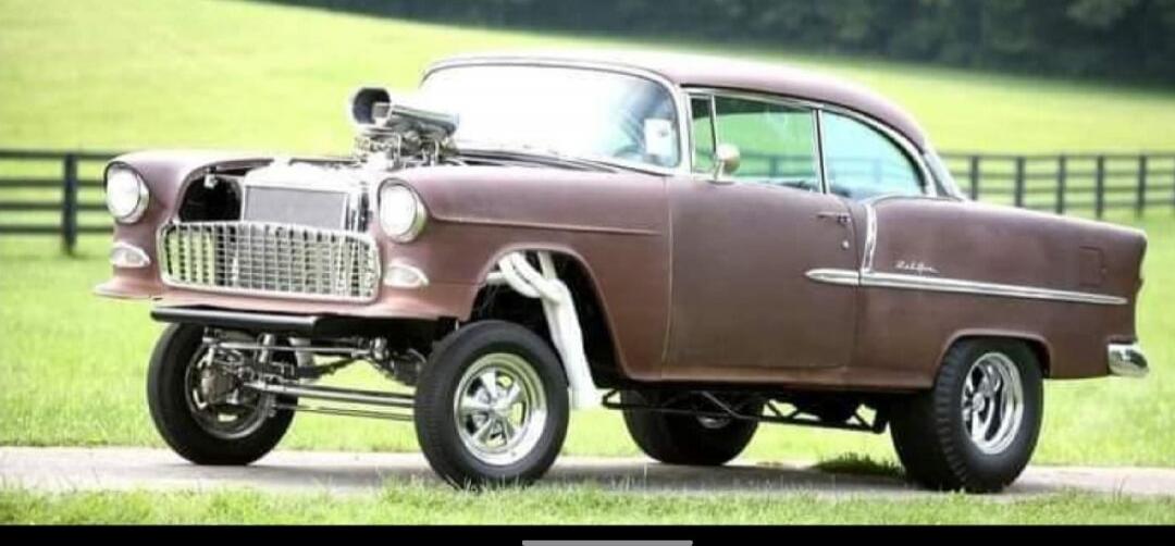 Session ID: 1060783.

image shows a vintage brown classic car, likely from the 1950s, parked on a road with a green field and fence in the background.