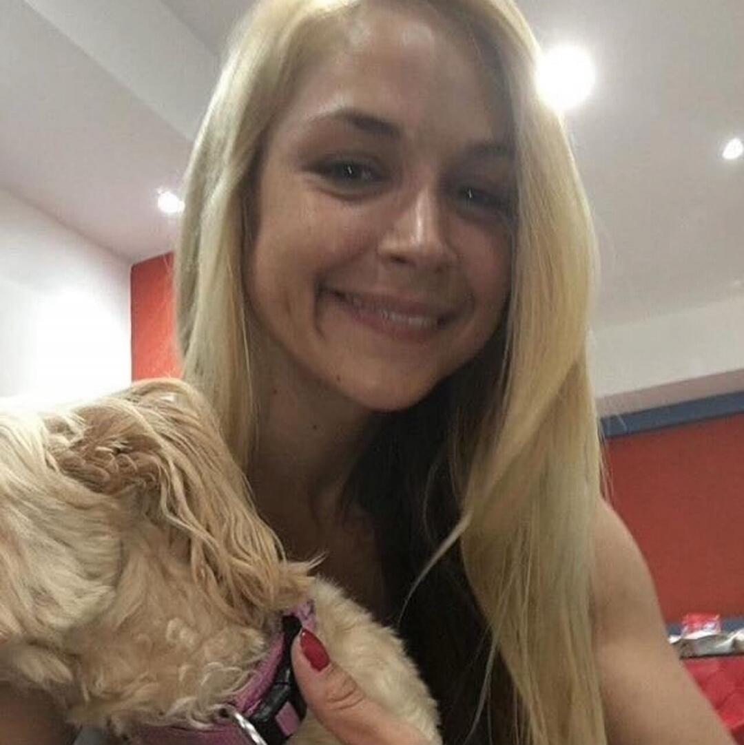 Smiling blonde woman holding a small fluffy dog indoors.