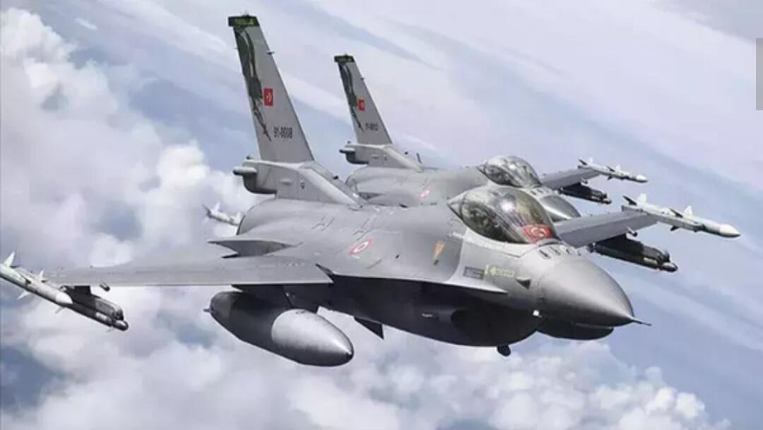 Two Turkish F-16 fighter jets are flying in formation against a cloudy sky. They are armed with missiles on their wings.