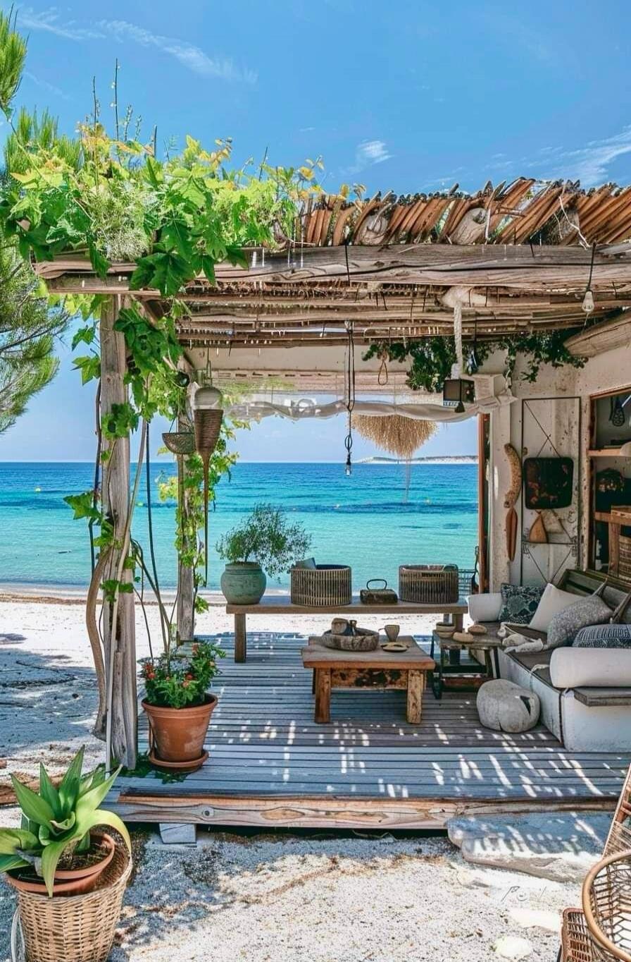 Beachside seating area with a thatched roof, wooden furniture, plants, and a view of the blue sea.