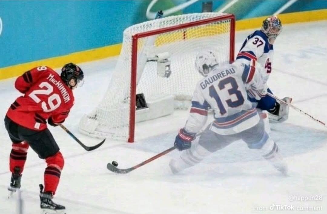 A hockey game scene: a player in a red jersey (number 29) is skating toward the goal with the puck, while a goalie in a white jersey (number 13) with the name Gaudreault on the back blocks the shot near the net.