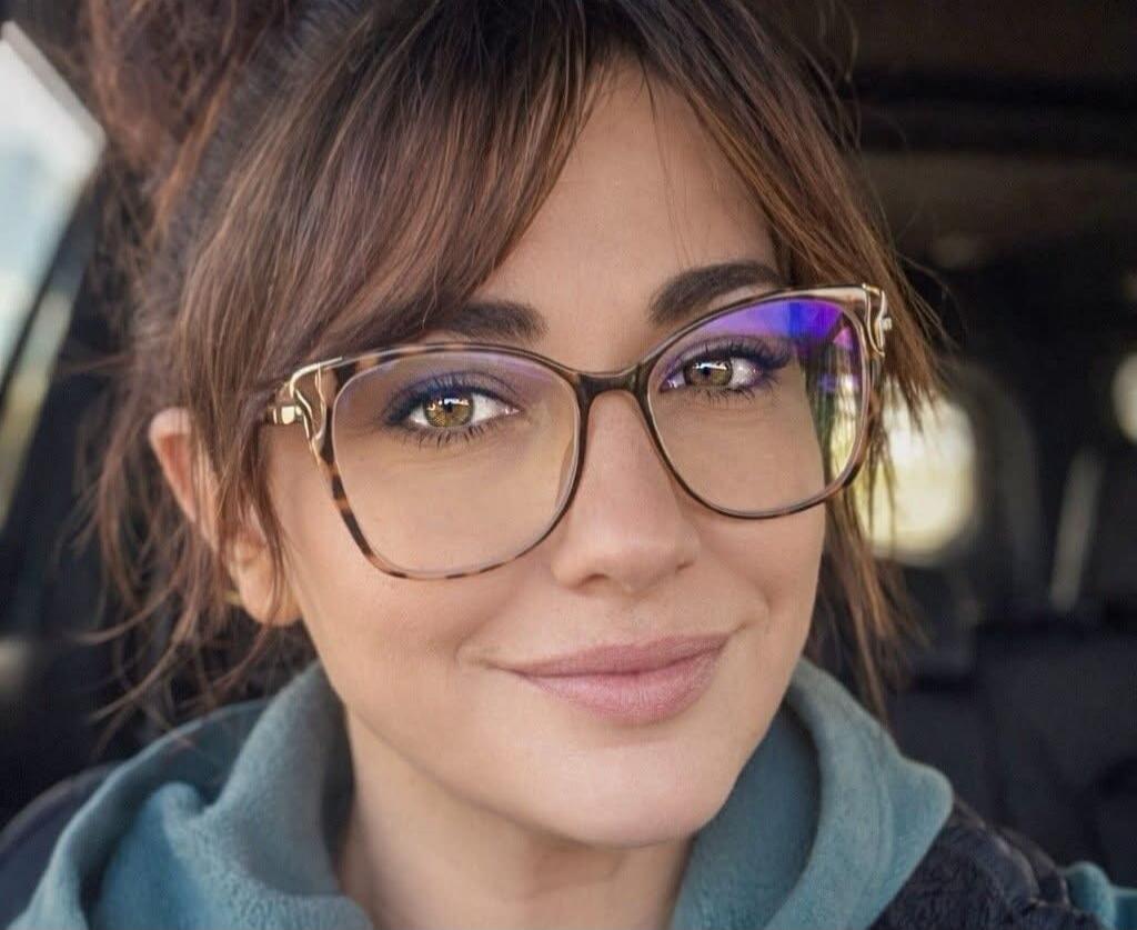 Portrait of a woman with brown hair and glasses, inside a car.