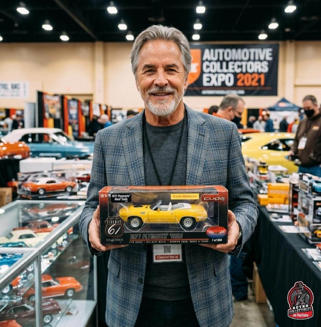 Don Johnson is seen holding a 1/18 scale model of a yellow 1971 Plymouth 'Cuda, associated with the TV show Nash Bridges. The model is a limited edition, 1 of 504, by Highway 61. In the background, a banner reads 'Automotive Collectors Expo 2021'.