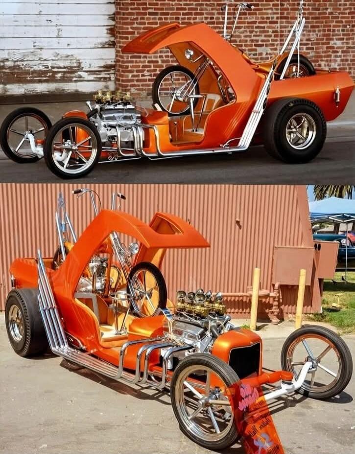 A unique custom-built orange hot rod with an exposed engine and chrome details. The car features a distinctive design with a raised canopy and what appears to be a bicycle integrated into the rear section. It is shown in two different angles against a brick wall and a corrugated metal background.