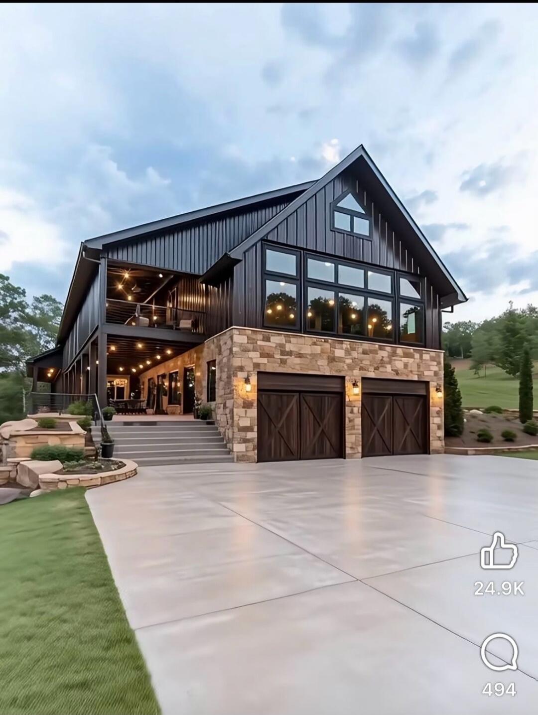Large modern house with dark exterior and stone accents, two-car garage, string lights along the porch. Social UI shows like count 24.9K and comments 494.
