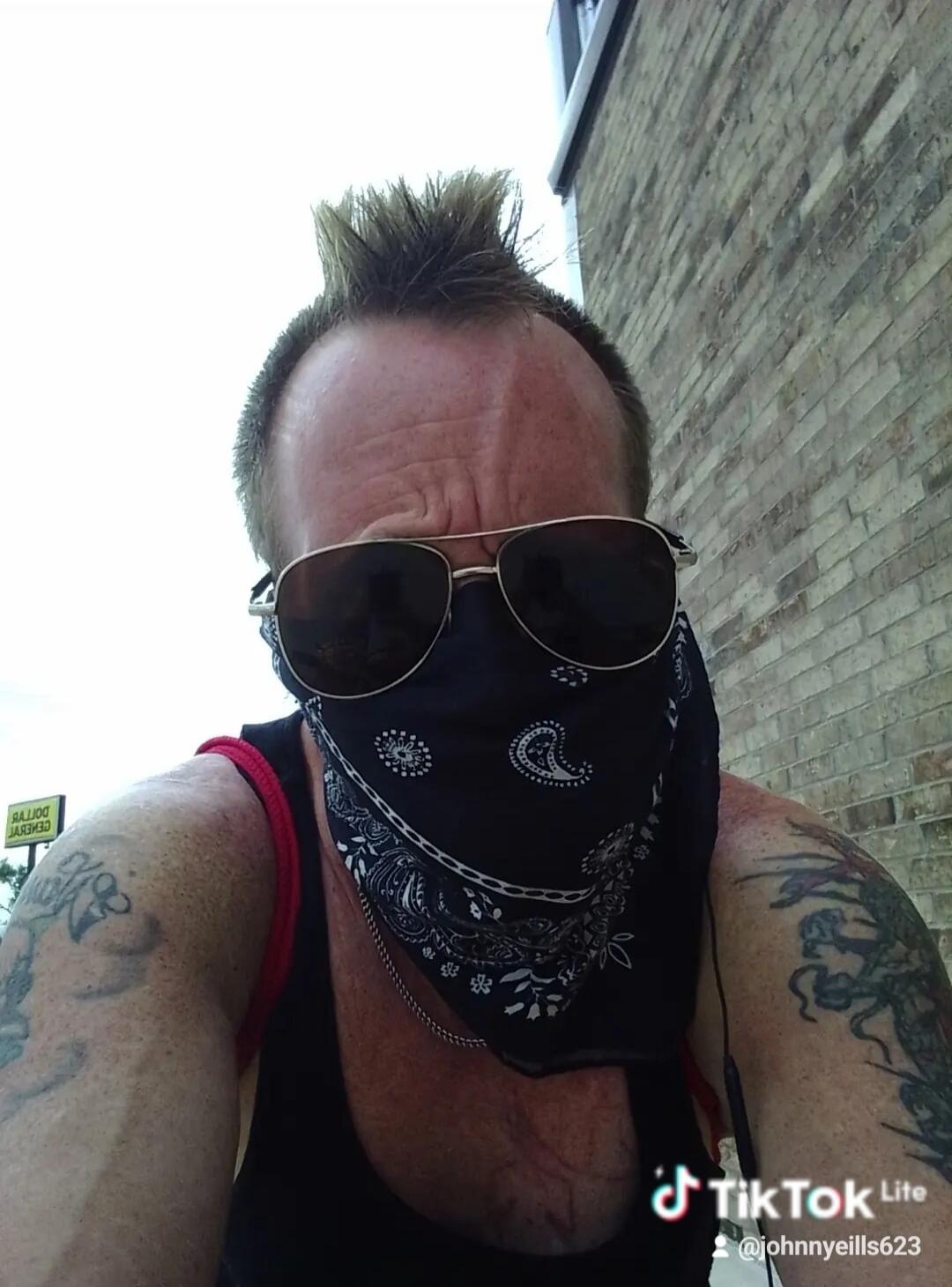 TikTok Lite @johnnyeills623. A person with a mohawk, sunglasses, and a bandana covering their face. A Dollar General sign is visible in the background.