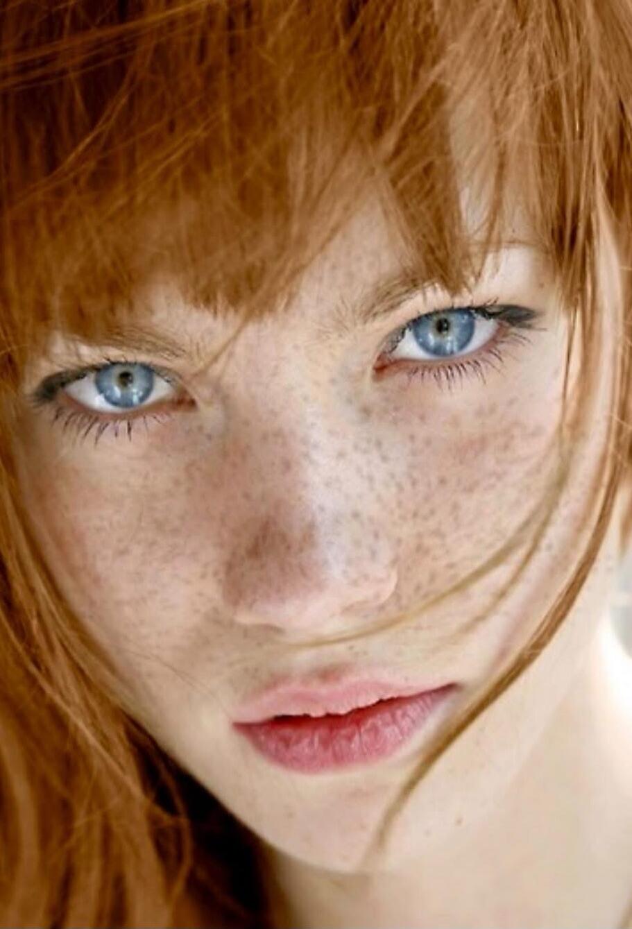 A close-up portrait of a red-haired person with blue eyes and freckles.