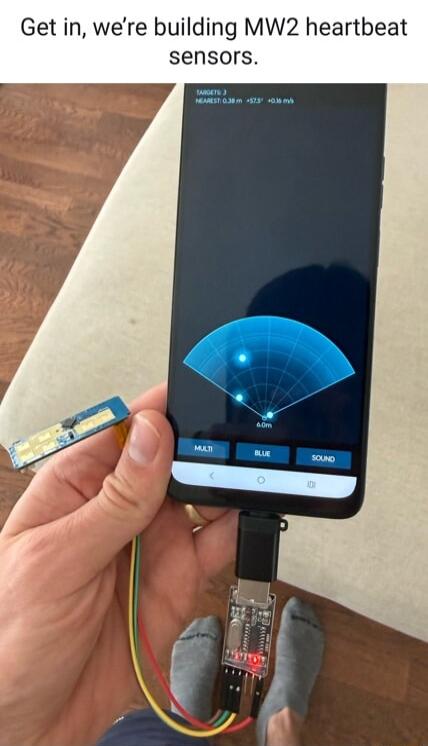 Get in, we're building MW2 heartbeat sensors. The phone screen displays a radar-like interface with 'TARGETS: 3', 'NEAREST: 0.38 m', and a blue fan-shaped display showing three dots, resembling a heartbeat sensor from Call of Duty: Modern Warfare 2. A small circuit board is connected to the phone via a USB-C adapter and wires.