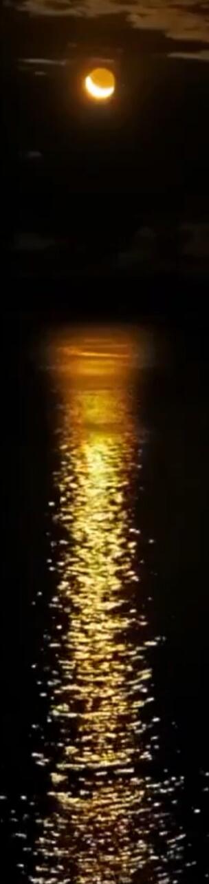 Bright orange moon over dark water, its golden reflection rippling across the surface.