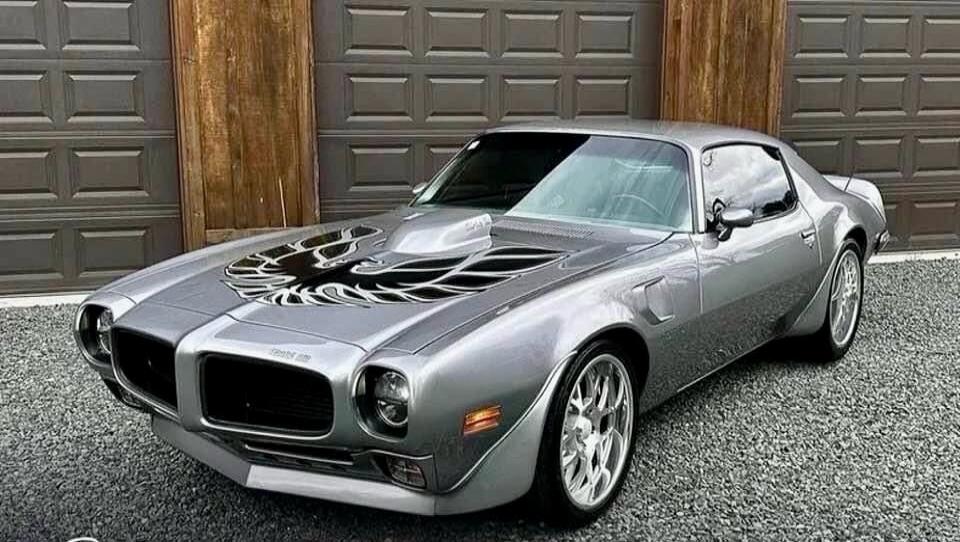 Classic silver Pontiac Firebird Trans Am with a black flame decal on the hood.