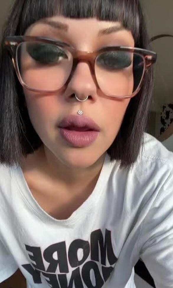 The text on the t-shirt is partially visible and mirrored, appearing to say 'MORE LOVE' or similar. The image shows a woman with glasses and facial piercings.