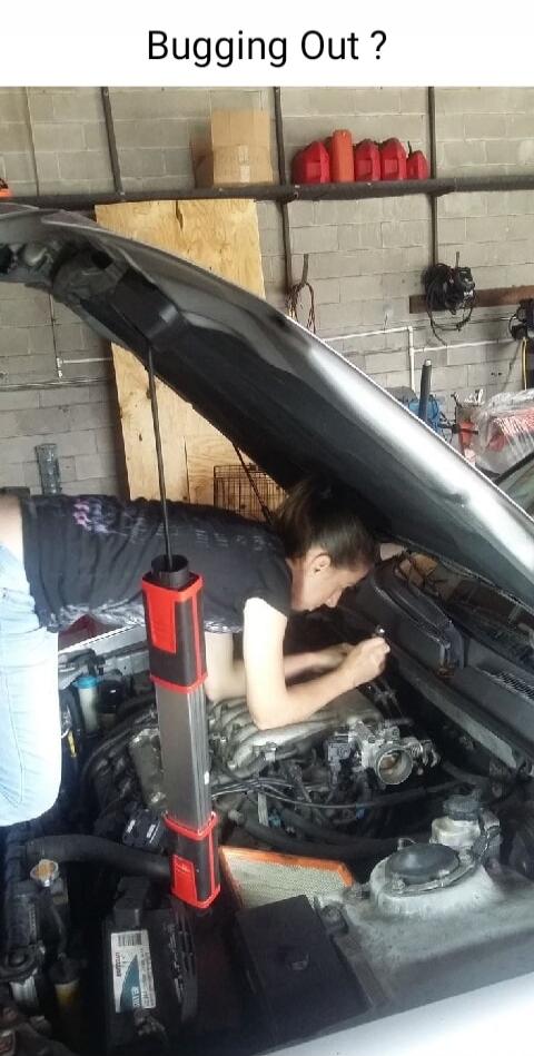 Bugging Out ? A person is deeply immersed in a car engine bay, suggesting an unusual or challenging repair situation.