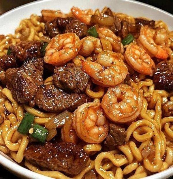 A close-up shot of a delicious stir-fried noodle dish with beef and shrimp, garnished with green onions.