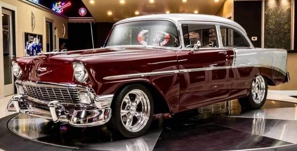 Classic American car, two-tone paint, chrome details, custom wheels. Text visible in reflection: 'AMERICAN WORK'. Neon sign in the background.