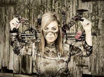 A woman in camouflage clothing with multiple chains and weapons strapped around her arms, making a fierce, grumpy face.