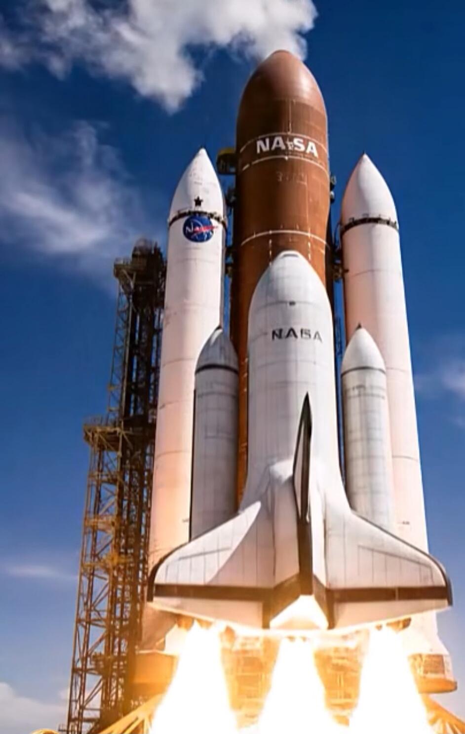 NASA on a space shuttle with large rocket boosters on a launch pad. The main shuttle is white with orange external tank and white boosters, with flames or ignition at the bottom.