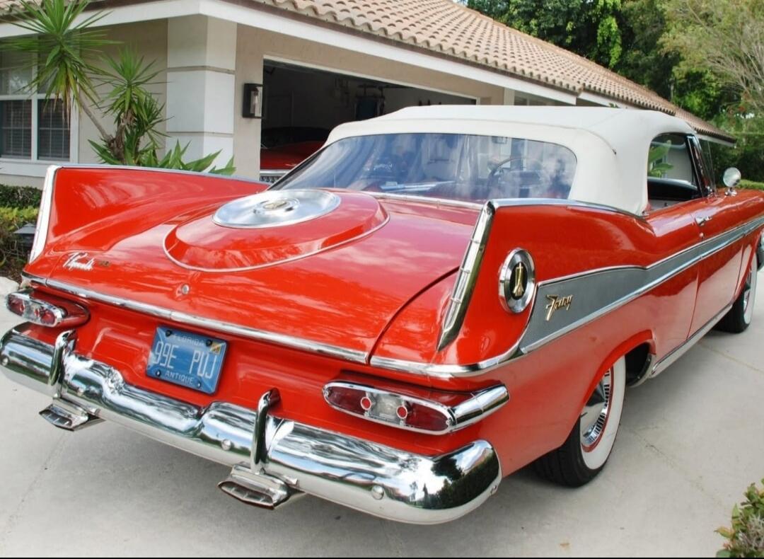 A classic red convertible car with a white soft top, prominent tail fins, and chrome details, parked on a driveway. The license plate reads 'FLORIDA 99E PUJ ANTIQUE'. The car appears to be a Plymouth Fury.
