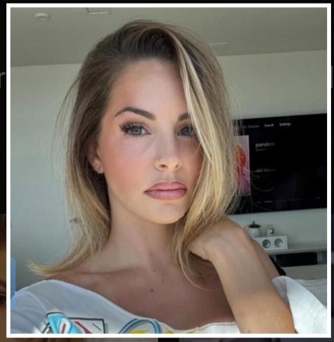 A woman with blonde hair and makeup looking at the camera. A TV screen is visible in the background with some text like 'pandora' and 'settings'.