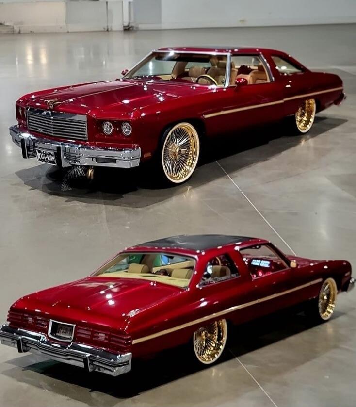 Two red vintage cars with tan interiors and gold spokes, displayed in a glossy showroom. Both vehicles are highly customized with chrome bumpers and lowered profiles.