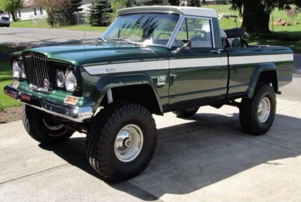 Classic green lifted pickup truck (Jeep Wagoneer/Commander style) with chrome bumper and off-road tires. It appears to be an older model with a two-tone paint job.